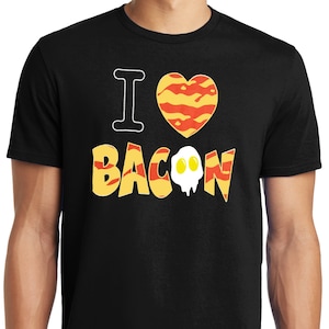 Puede incluir: Camiseta negra con el texto "I love bacon" en letras amarillas y naranjas. Un gr&aacute;fico en forma de coraz&oacute;n con un patr&oacute;n de tocino est&aacute; por encima del texto. Un gr&aacute;fico de huevo est&aacute; dentro de la palabra "bacon".