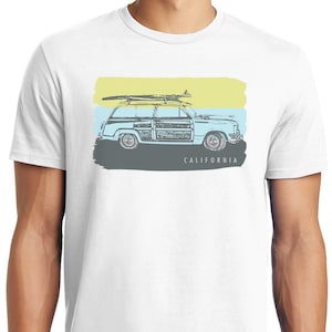 May include: White t-shirt with a vintage illustration of a station wagon with a surfboard on top. The car is driving on a road with a blue, green, and yellow painted background. The text "CALIFORNIA" is printed below the car.