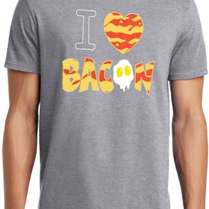 Puede incluir: Camiseta gris con el texto "Me encanta el bacon" en una fuente estilizada. La palabra "bacon" est&aacute; compuesta por tiras de tocino y un huevo frito.