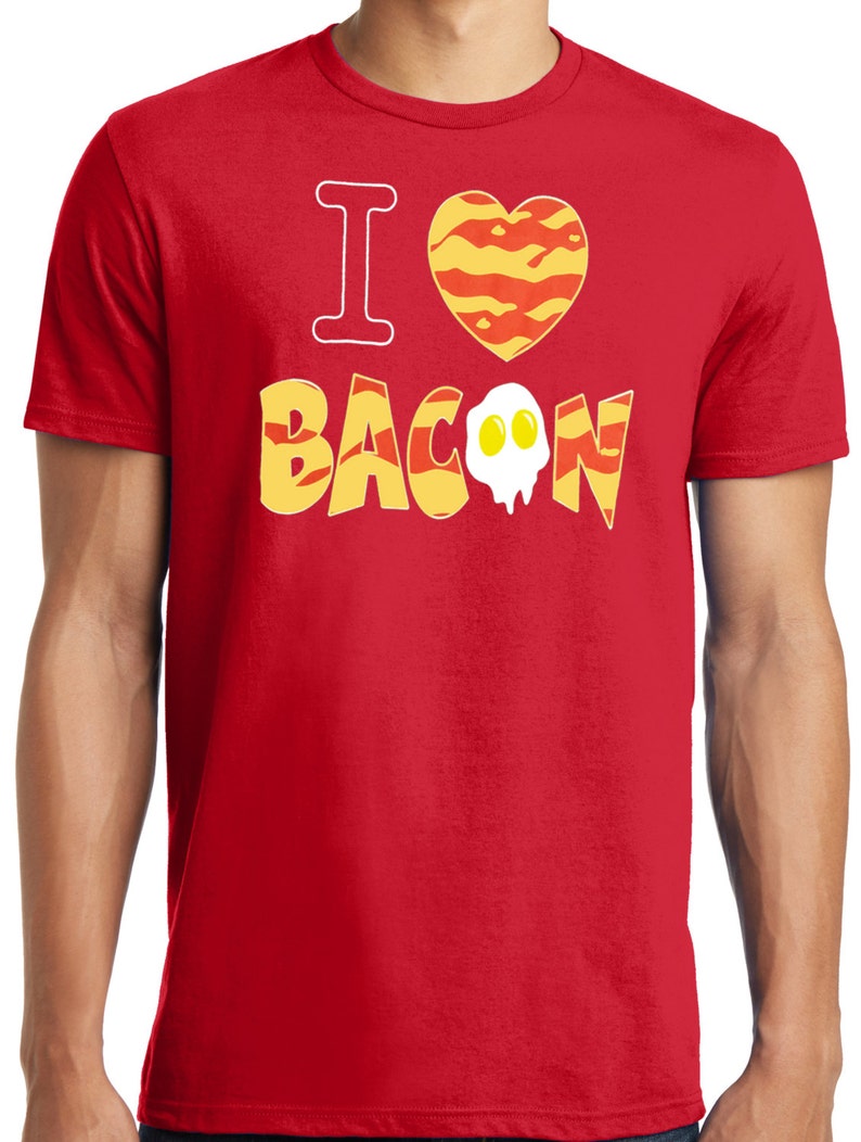 Puede incluir: Camiseta roja con el texto "Me encanta el bacon" en letras amarillas y naranjas. El coraz&oacute;n est&aacute; hecho de rayas de bacon y tiene un huevo frito encima.