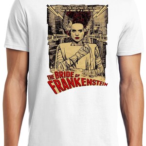 Puede incluir: Una camiseta blanca con un gr&aacute;fico de estilo vintage de la Novia de Frankenstein. El gr&aacute;fico presenta a una mujer con cabello verde y puntadas, vistiendo un vestido blanco y vendas. El texto "The Bride of Frankenstein" est&aacute; en letras rojas y blancas.