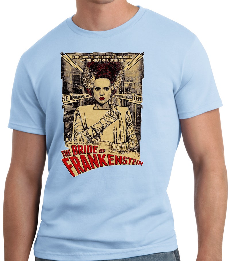 Puede incluir: Una camiseta azul claro con un dise&ntilde;o de p&oacute;ster vintage con la Novia de Frankenstein. El p&oacute;ster tiene el texto "The Bride of Frankenstein" y "Made from the skeletons of two women and the heart of a living girl."