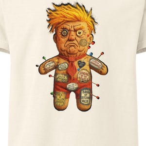 May include: Off-white t-shirt featuring a cartoon voodoo doll with orange hair and a red tie. The doll has pins and labels with text like "Binding of the Bowels" and "Hex Fallen Stocks".