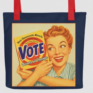 May include: Navy blue tote bag with red handles. The bag features a vintage-style graphic of a smiling woman holding a box labeled "VOTE" with the text "Oceans of Change". The design has a retro aesthetic.