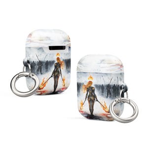 May include: A white Airpods case with a colorful design featuring a woman with a crown of fire walking towards a line of soldiers. The case has a silver metal keychain attached.