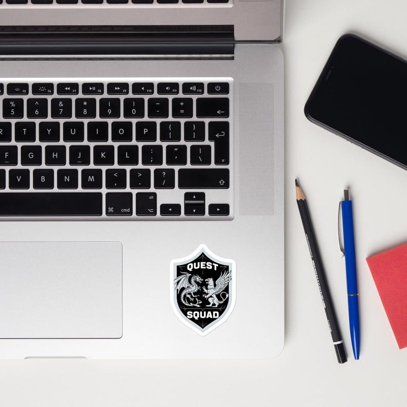 May include: A black and white sticker with a shield design. The shield has a dragon and a lion inside. The text "QUEST SQUAD" is on the shield.