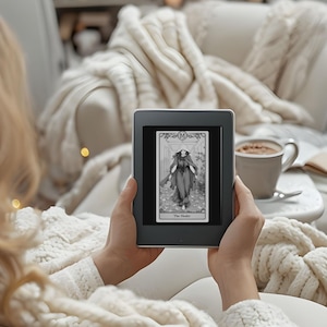 May include: A person is holding a black and white e-reader displaying a tarot card with the image of a woman in a long robe and the text "The Healer".