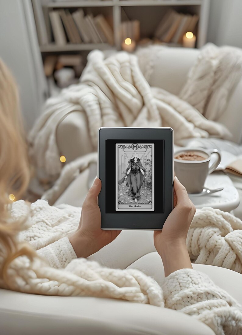 May include: A person is holding a black and white e-reader displaying a tarot card with the image of a woman in a long robe and the text "The Healer".