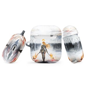 May include: A white Airpods case with a watercolor design of a woman holding two flaming torches, walking away from a crowd of people. The design is in shades of gray, white, and orange.