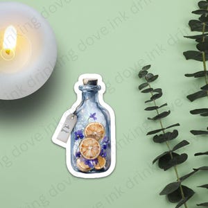 Op de afbeelding: Een blauwe glazen fles met een kurkstop, gevuld met gedroogde sinaasappelschijfjes en paarse bloemen. De fles heeft een wit label met de tekst "Just Breathe" erop.