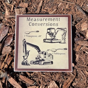 May include: Square sign with the text "Measurement Conversions" and illustrations of construction vehicles and spoons. The sign shows the conversion of 1 teaspoon to a construction vehicle and 1 tablespoon to a construction vehicle.