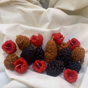 May include: A collection of small, hand-crafted candles shaped like raspberries, blackberries, and blueberries. The candles are made of natural wax and have a realistic appearance.