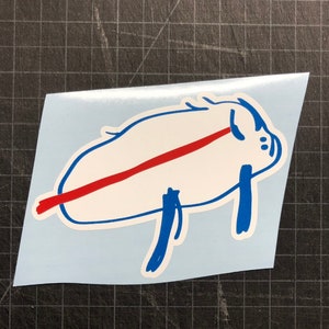 May include: A white sticker with a blue outline of a pig with a red line across its body. The pig is lying on its side with its legs in the air.