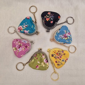 May include: Six floral patterned coin purses with keyrings. Each purse has a different floral pattern and colour, including pink, blue, green, and yellow. The purses are made of fabric and have a metal frame.