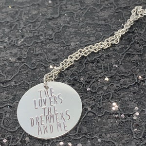 May include: Silver necklace with a round pendant that says "The Lovers The Dreamers And Me".