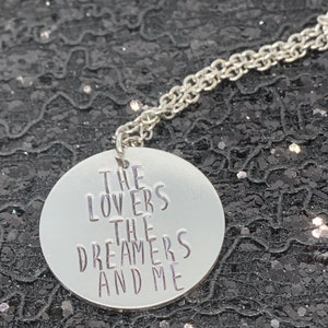 May include: A silver necklace with a round pendant that says "The Lovers The Dreamers And Me".