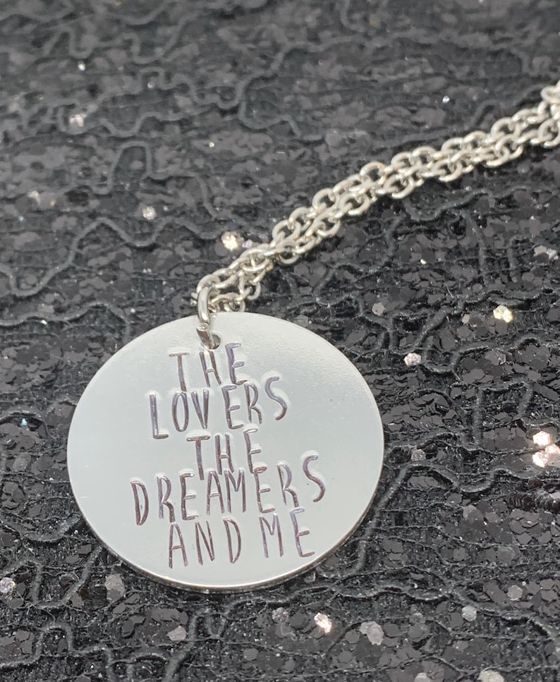 May include: A silver necklace with a round pendant that says "The Lovers The Dreamers And Me".