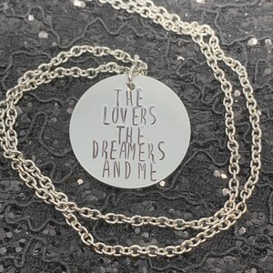 May include: Silver necklace with a round pendant that says "The Lovers The Dreamers And Me".