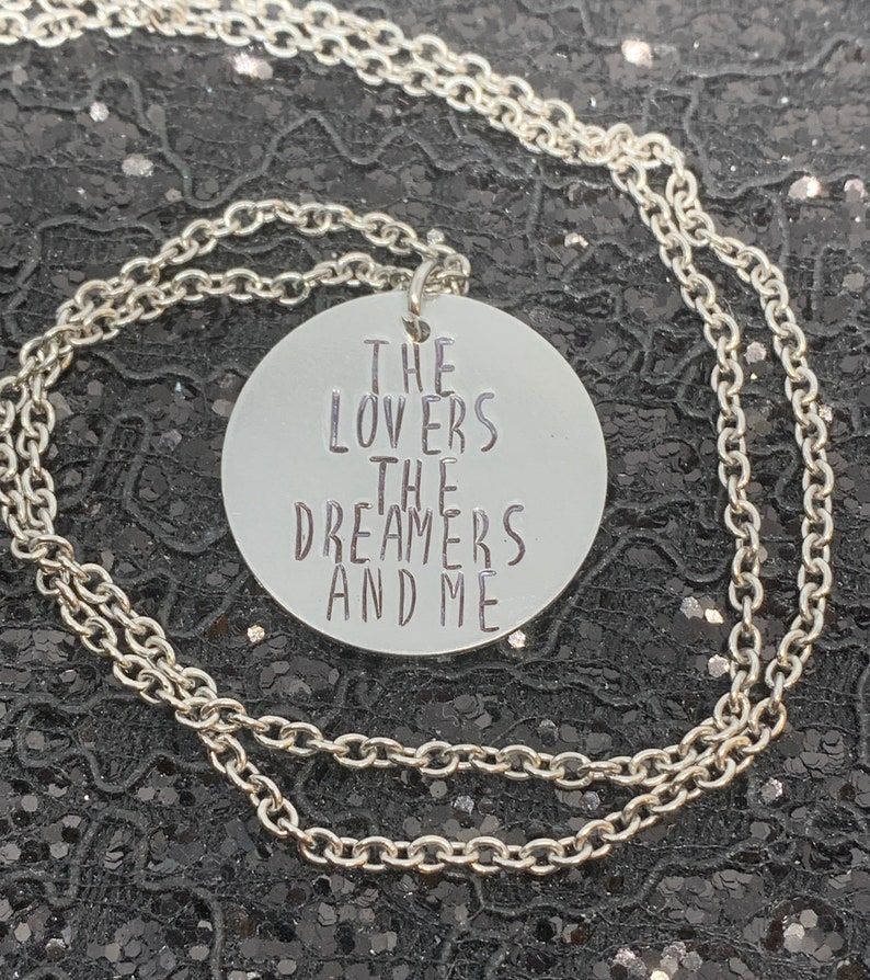 May include: Silver necklace with a round pendant that says "The Lovers The Dreamers And Me".