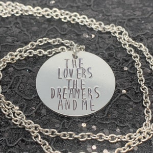 May include: Silver necklace with a round pendant that says "The Lovers The Dreamers And Me".
