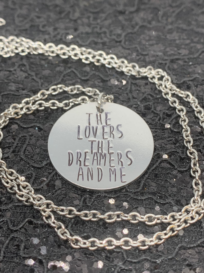 May include: Silver necklace with a round pendant that says "The Lovers The Dreamers And Me".