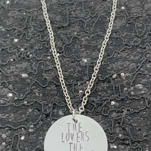 May include: A silver necklace with a round pendant that says "The Lovers The Dreamers And Me".