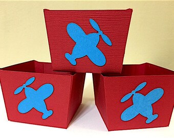 Puede incluir: Tres cajas de cartón rojo con recortes de aviones azules. Las cajas están apiladas una encima de la otra.