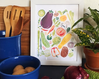 May include: A framed watercolor print of various vegetables, including eggplant, carrots, and zucchini. A blue ceramic bowl holds potatoes, and a red onion rests on a green cloth. Wooden utensils are in a blue utensil holder.