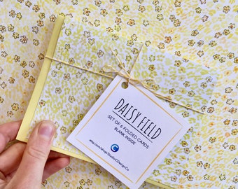 May include: A set of six folded blank cards with a yellow daisy field pattern. The cards are tied together with twine and have a white tag that reads "DAISY FIELD, SET OF 6 FOLDED CARDS, BLANK INSIDE, etsy.com/shop/StudioCDesignCo".