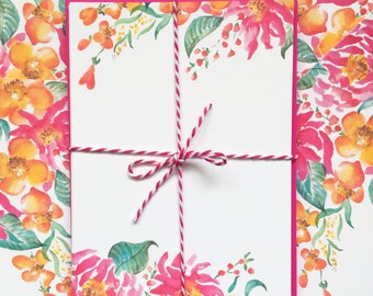 May include: Two white note cards with pink borders are tied together with a white and red twine bow. The cards are decorated with a watercolor floral border of pink and yellow flowers.