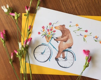 May include: A watercolor illustration of a brown bear riding a blue bicycle with a basket of flowers. The bear is wearing a brown fur coat and has a happy expression on its face. The bicycle has a blue frame and white wheels. The flowers in the basket are yellow, pink, and purple.