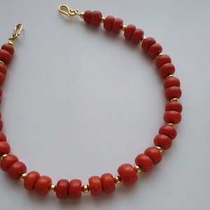 May include: A red coral necklace with gold beads and clasps. The necklace is made of round coral beads and has a simple design.