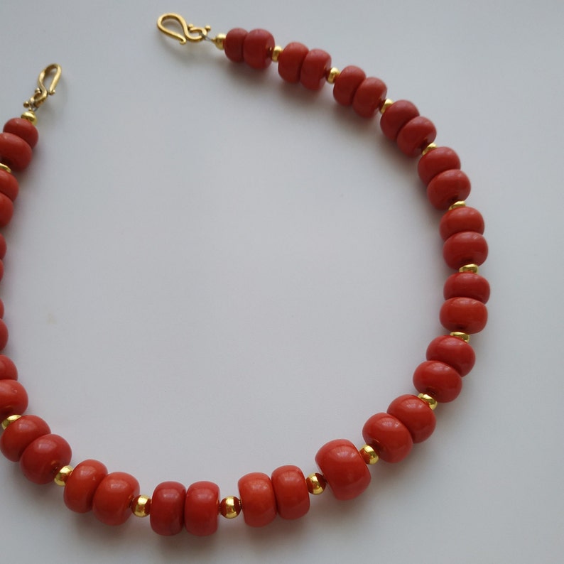 May include: A red coral necklace with gold beads and clasps. The necklace is made of round coral beads and has a simple design.