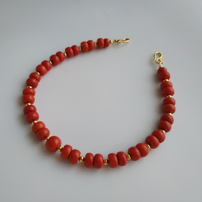 May include: A red coral bead bracelet with gold accents and a lobster clasp closure.