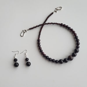 May include: A set of garnet jewelry featuring a necklace and earrings. The necklace is made of dark red garnet beads and silver clasps. The earrings are silver with dark red garnet beads.
