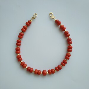 May include: A red coral beaded necklace with gold clasps. The necklace is made of small, round beads and is approximately 18 inches long.