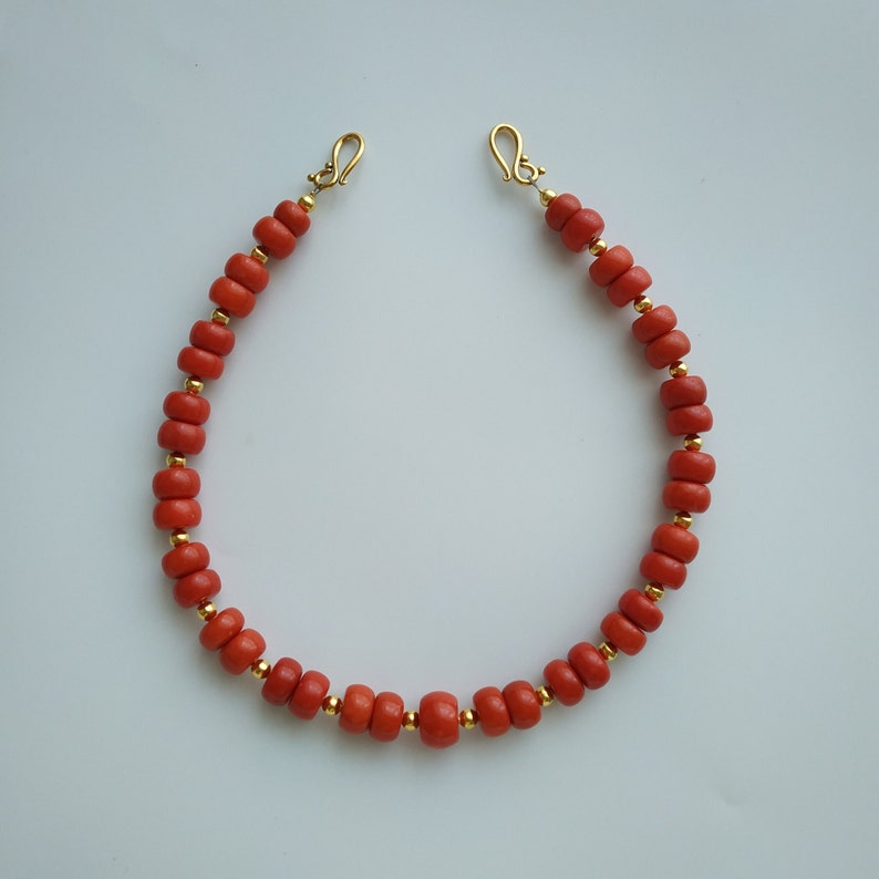 May include: A red coral beaded necklace with gold clasps. The necklace is made of small, round beads and is approximately 18 inches long.