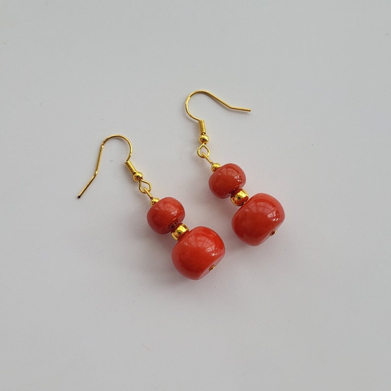 May include: A pair of dangle earrings with two red round beads on each earring. The earrings have gold hooks.