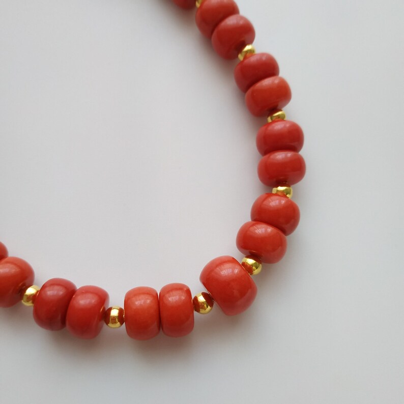May include: A red coral beaded necklace with gold spacers. The necklace is made of round beads and is strung on a gold chain.