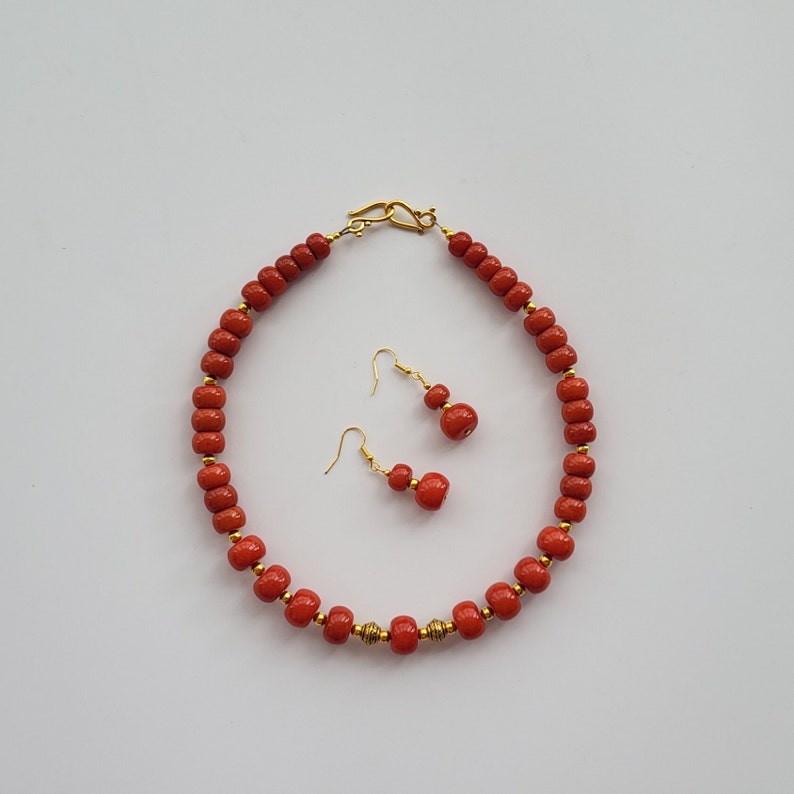 May include: A red coral bead necklace with gold accents and matching earrings. The necklace is made of round beads and has a clasp closure. The earrings are dangle earrings with a single red coral bead.