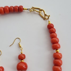 May include: A red coral necklace with a gold clasp and matching earrings. The necklace is made of round beads and the earrings are dangle style.