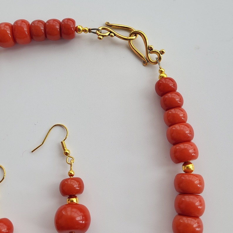 May include: A red coral necklace with a gold clasp and matching earrings. The necklace is made of round beads and the earrings are dangle style.