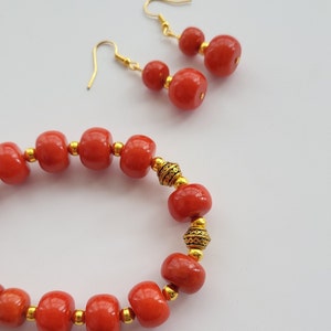 May include: A red coral bead bracelet with gold accents and matching earrings. The bracelet has a simple design with round beads and gold spacers. The earrings are also made with red coral beads and gold accents.