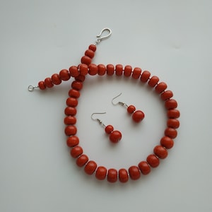 May include: A set of orange bead jewelry, including a necklace and earrings. The necklace is made of large, round beads and has a silver clasp. The earrings are also made of orange beads and have silver hooks.
