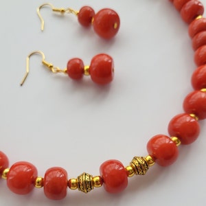 May include: A red and gold beaded necklace and earrings set. The necklace is made of round red beads with gold accents. The earrings are made of three red beads with gold accents.