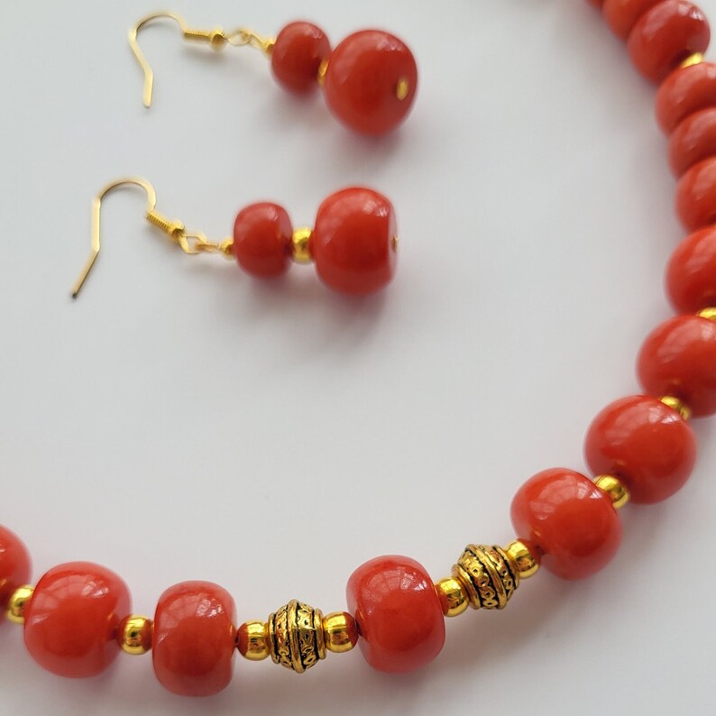 May include: A red and gold beaded necklace and earrings set. The necklace is made of round red beads with gold accents. The earrings are made of three red beads with gold accents.
