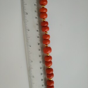 May include: A strand of coral beads with gold accents. The beads are approximately 1/2 inch in diameter and are strung on a clear cord.