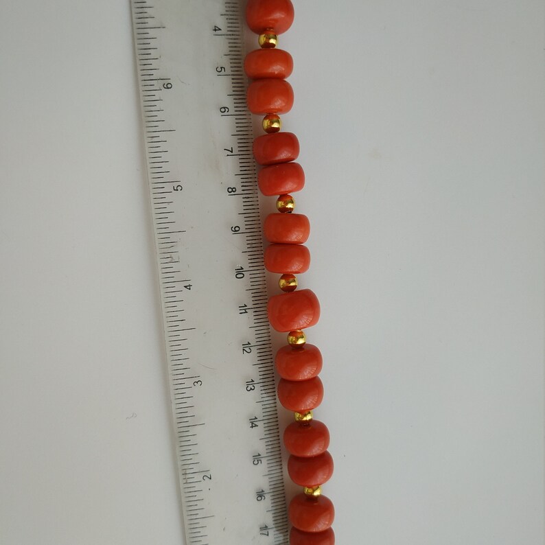 May include: A strand of coral beads with gold accents. The beads are approximately 1/2 inch in diameter and are strung on a clear cord.