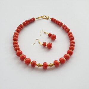 May include: A red coral bead necklace and matching earrings. The necklace is made of round beads with gold accents. The earrings are also made of red coral beads with gold accents.