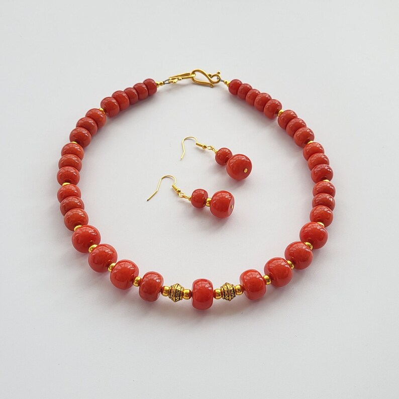 May include: A red coral bead necklace and matching earrings. The necklace is made of round beads with gold accents. The earrings are also made of red coral beads with gold accents.